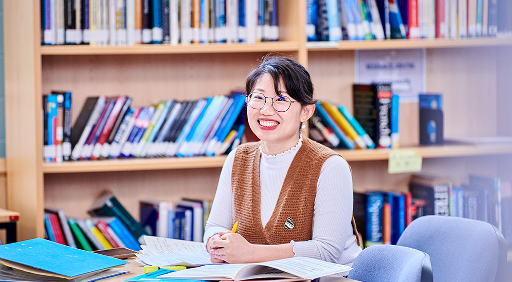 Student working at a desk with books in the background